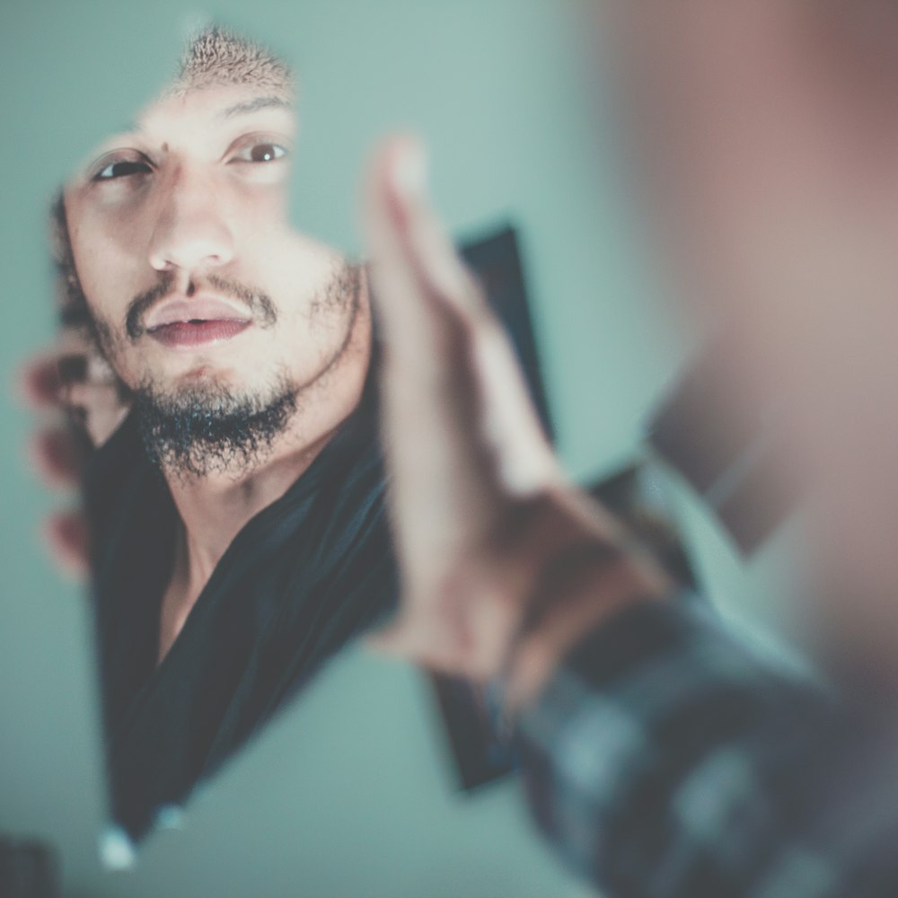 انعكاس وجه رجل غائم في مرآة قديمة بجانب صورة على الجدار