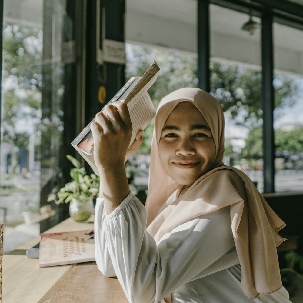 امرأة محجبة تمسك كتابا أمام وجهها وسط أكوام الكتب